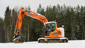 Orange excavator on snowy ground with pine trees in the background